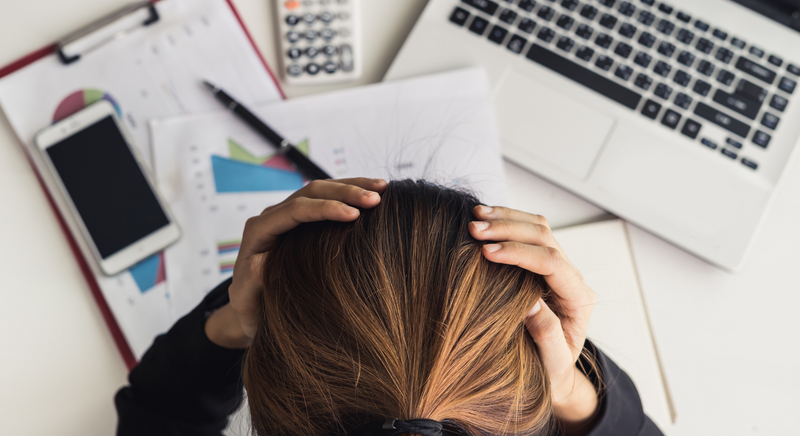 Blonde woman with head in her hands, stressed at work desk