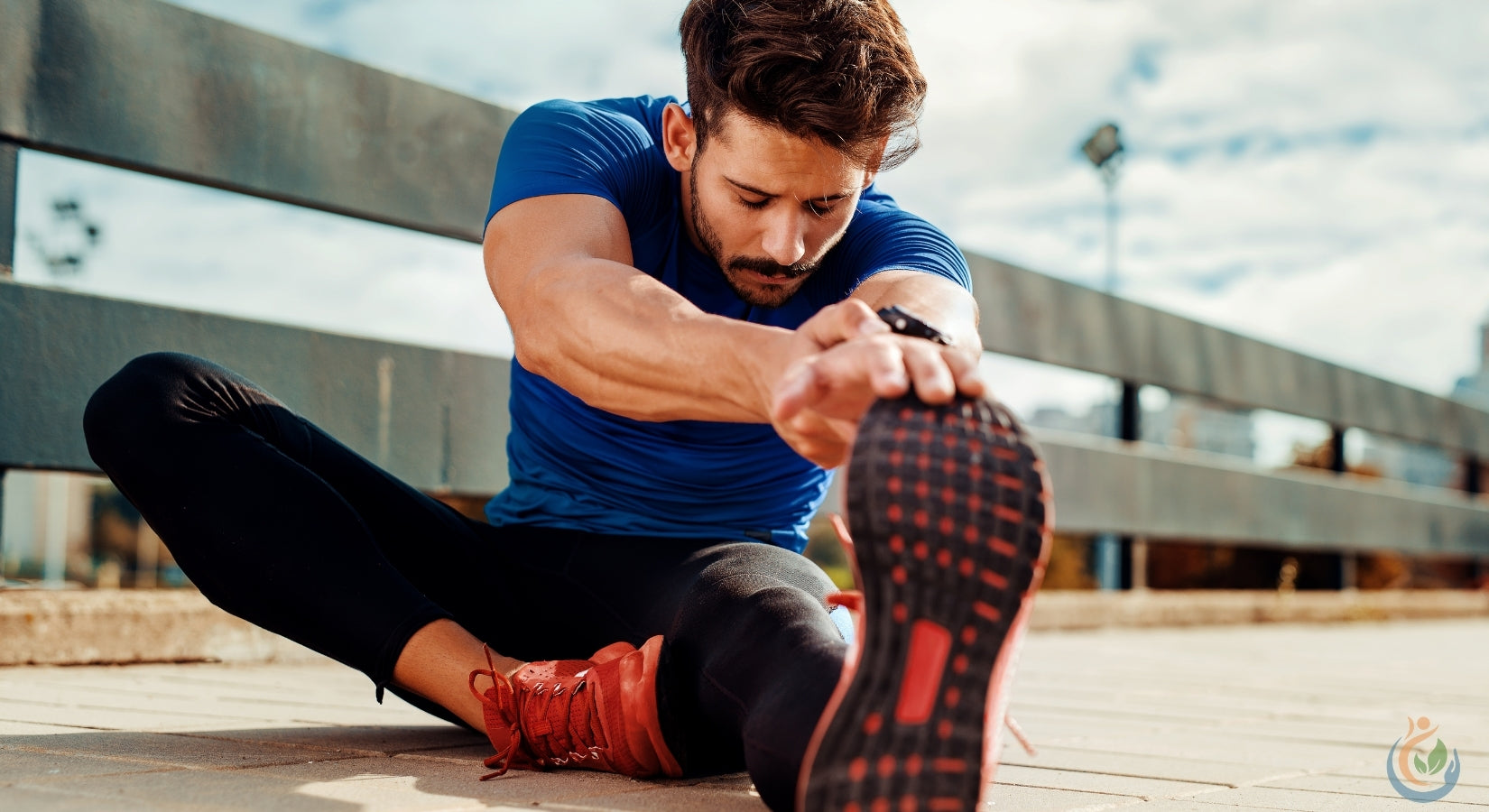 muscular man stretching on the ground outdoors in blue shirt and running shoes