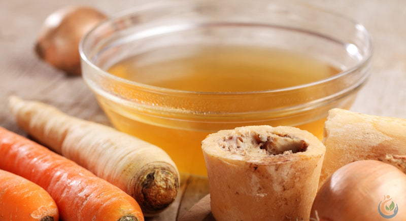 clear glass bowl of bone broth on table with carrots and onions