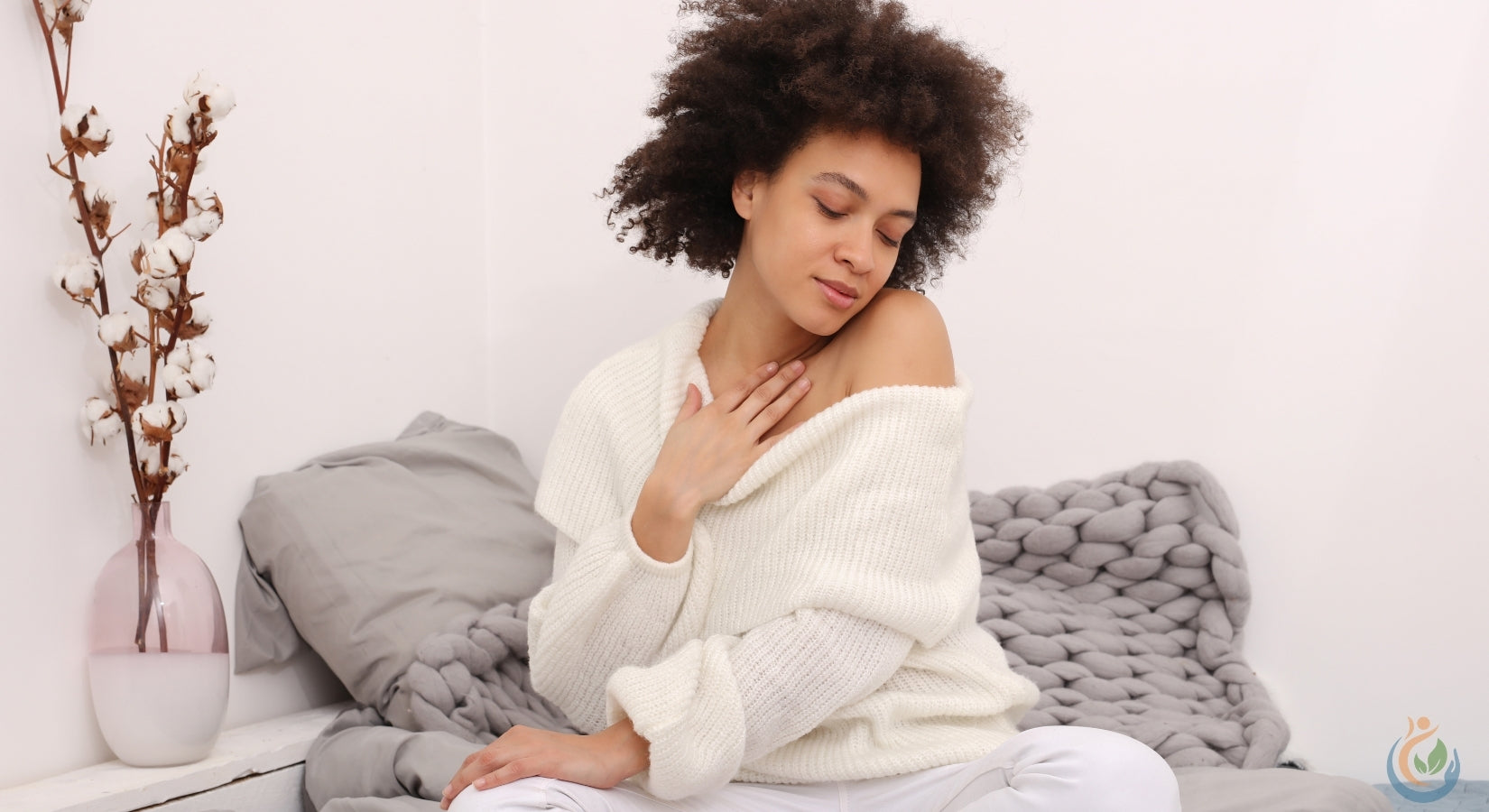 Beautiful woman with dark short curly hair comfy in bed with cream sweater and grey knitted blanket