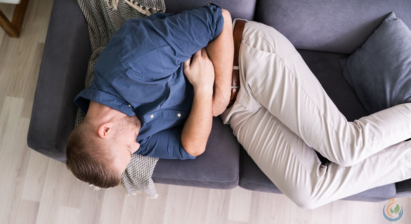 Man in nice clothes on grey couch holding stomach in pain